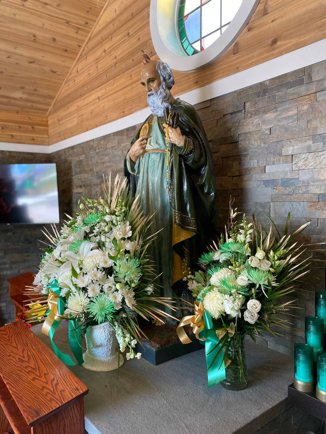 Inside the shrine, a statue of St. Jude stands over green and white flowers.